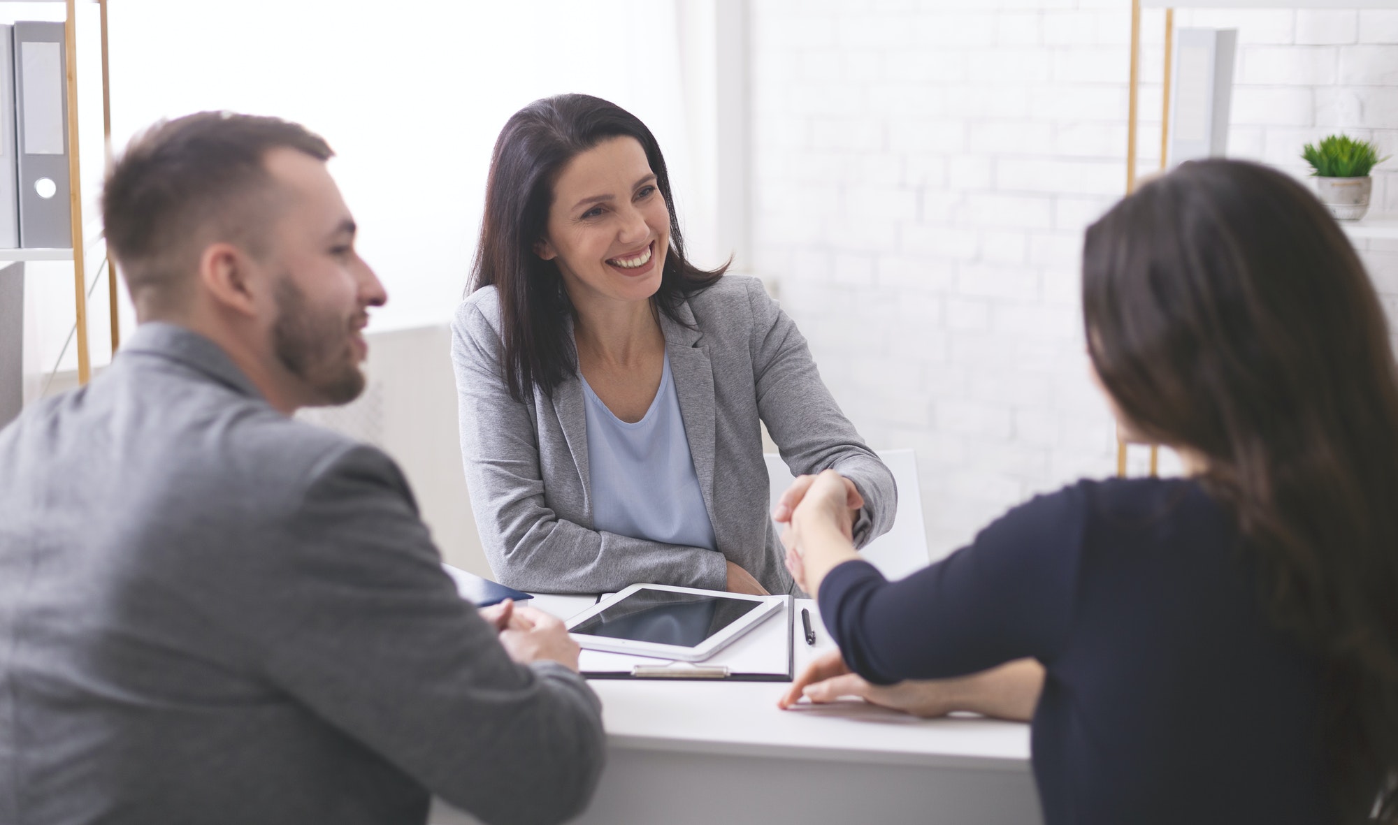 Positive insurance broker handshaking with young couple